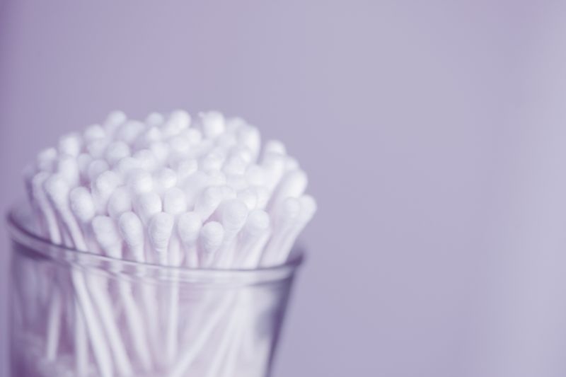 A clear canister full of new cotton swabs sits in front of a light gray background.