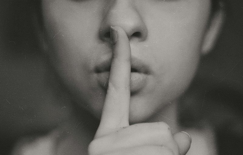 The lower part of someone's face, with their index finger to their lips in a 