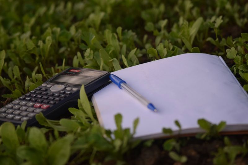 A notebook, pen, and calculator on a field of grass.