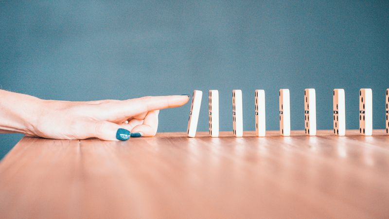 A hand tipping over a set of dominoes.