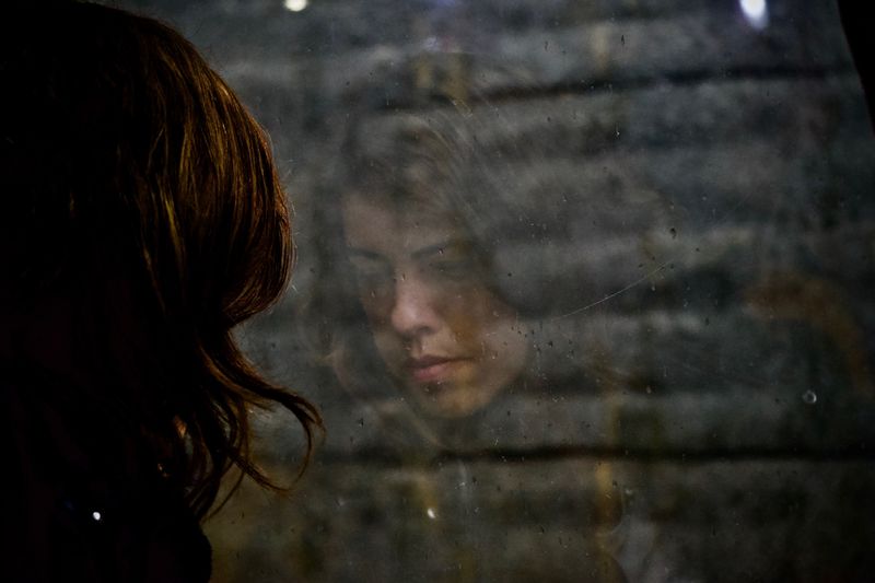 Woman's looking down; her reflection is a glass