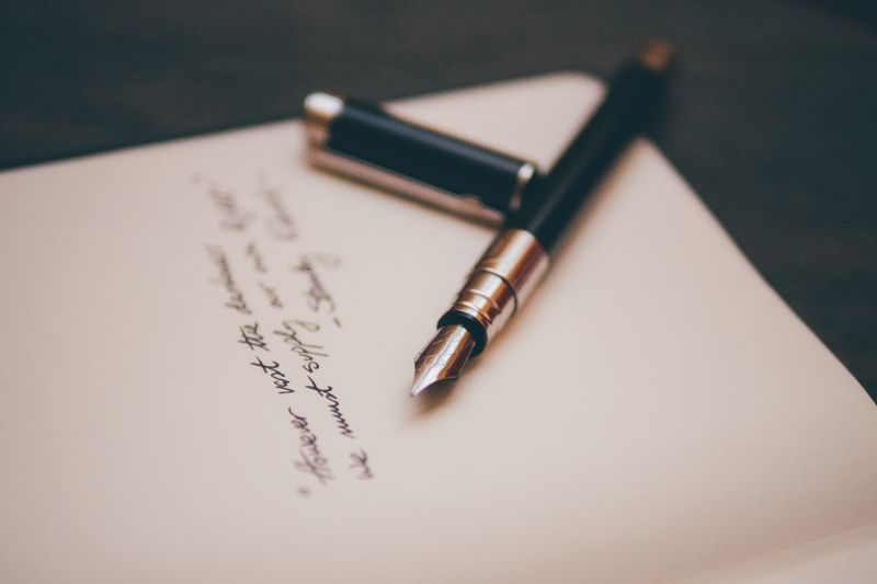 A fountain pen laying on top of a paper. The cap of the pen is off and is placed on side. 