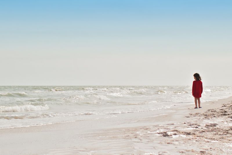 A child alone on a beach looking at the waves