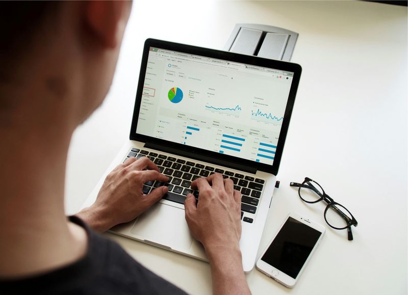 A person working on a laptop, viewed from their perspective, with graphs and charts displayed on the screen