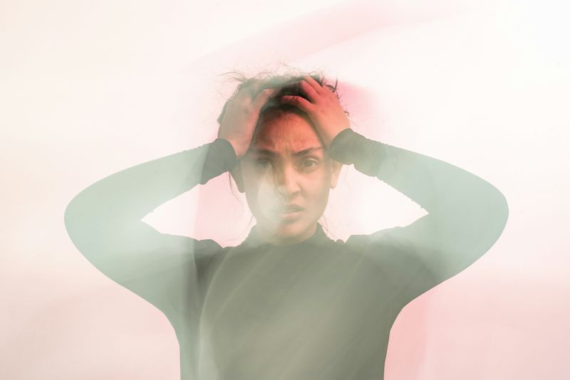 A person with hands on their head, anxious expression, partially covered by a foggy pink light.