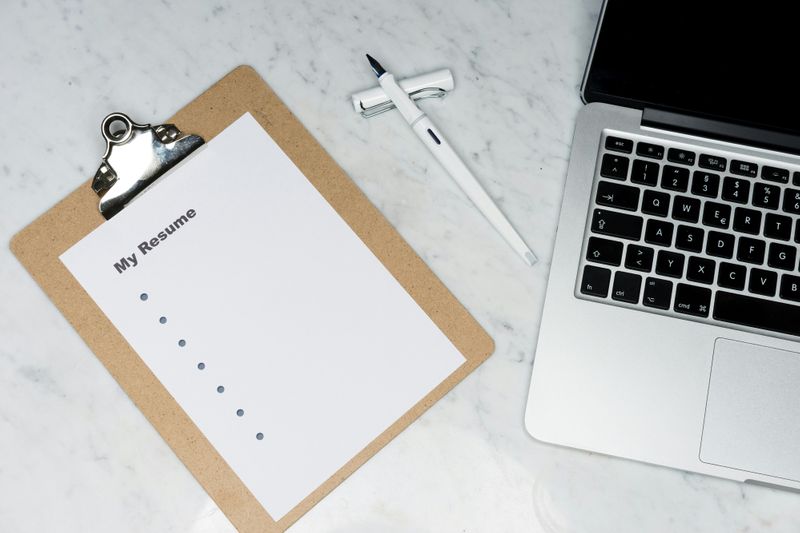 A computer next to a clipboard with notes for a resume on it