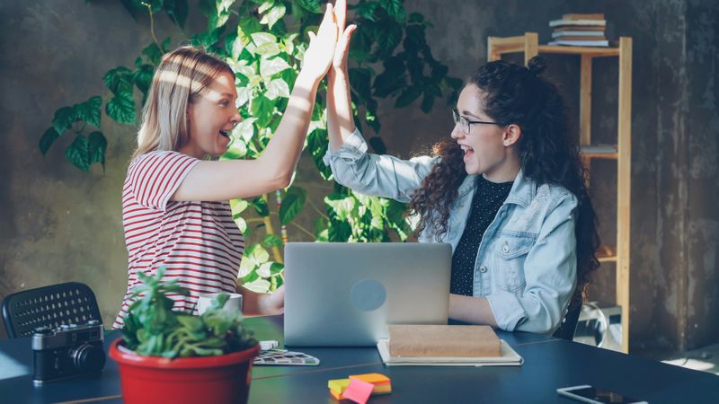 Two women high fiving each other while smiling.
