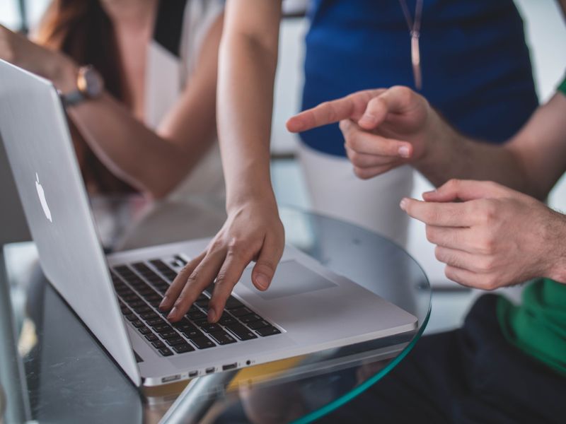 Laptop on table with several pairs of hands working on the same device