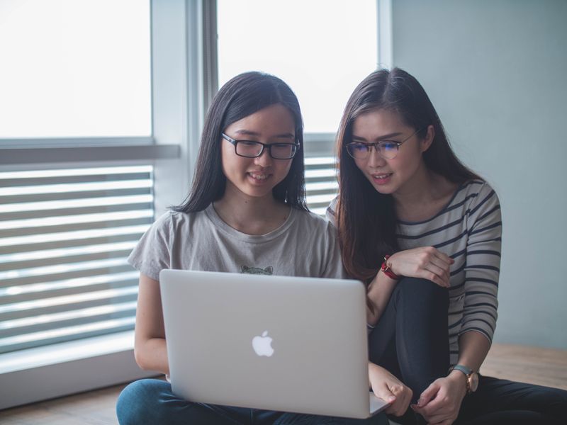 Two young female students research together on a laptop.