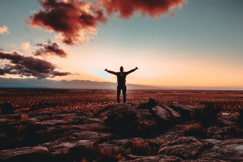 Someone standing on a rock during sunset with their arms stretched up in the sky.