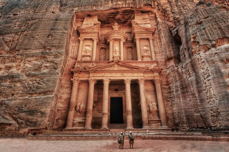 Two tourists looking up at the entrance to Petra in Jordan.