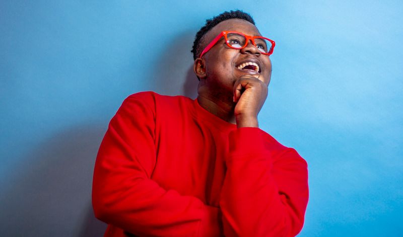 A Black man wearing red, thinking happily.