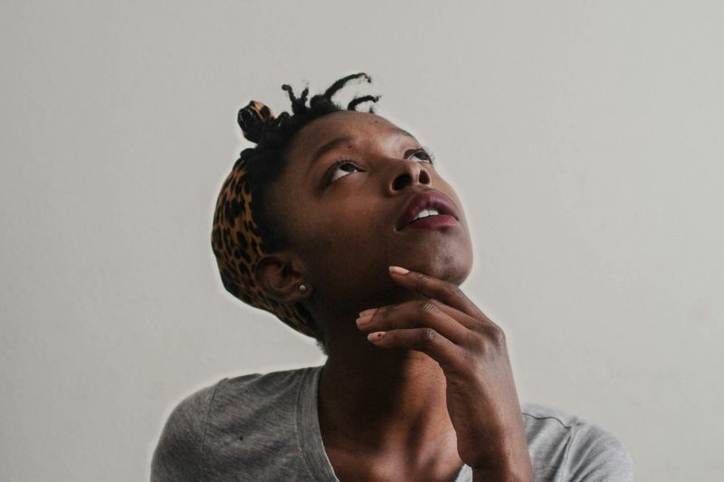 A young woman looking thoughtfully upwards, with her hand near her chin. 