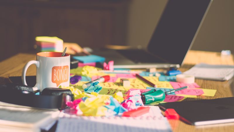 A desk with papers, pens, notebooks, and other items all over it.