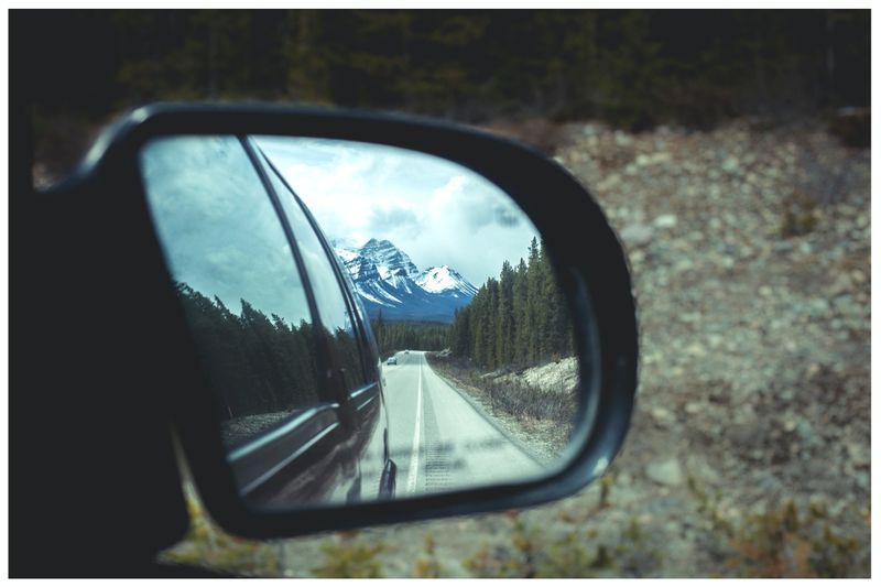 The reflections of a mountain and highway are seen in the side-view mirror of a vehicle.