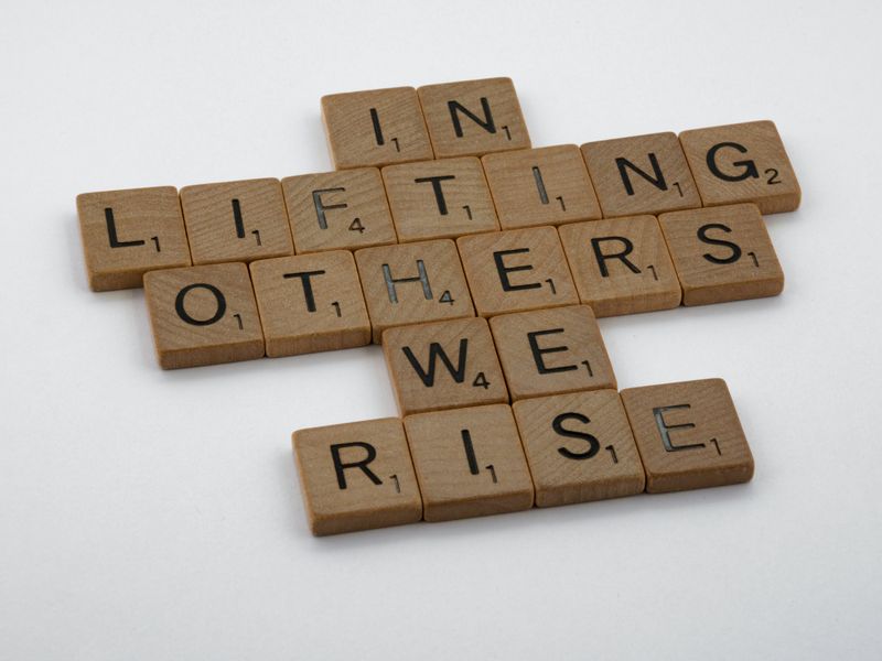 Scrabble letters spelling the phrase, in lifting others we rise.