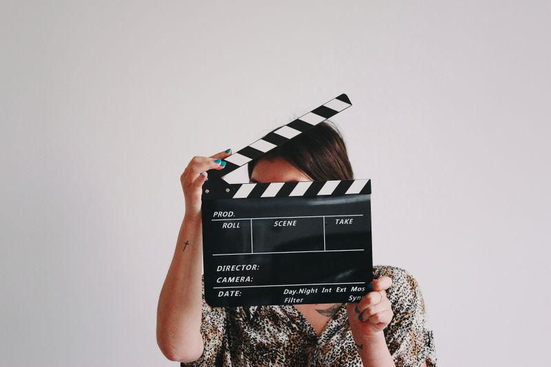 Image of woman holding a clapperboard covering her face. 