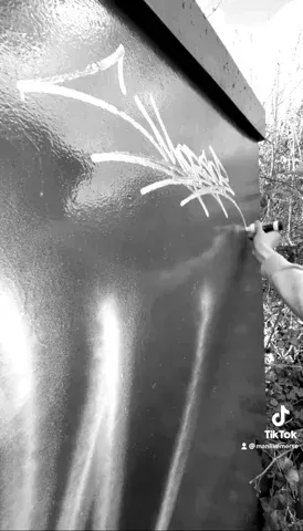 The arm of a person tagging their signature on a surface, using a white marker, as a train passes by in the background.