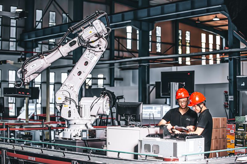 A robotic arm in a warehouse operated by two manufacturing workers.