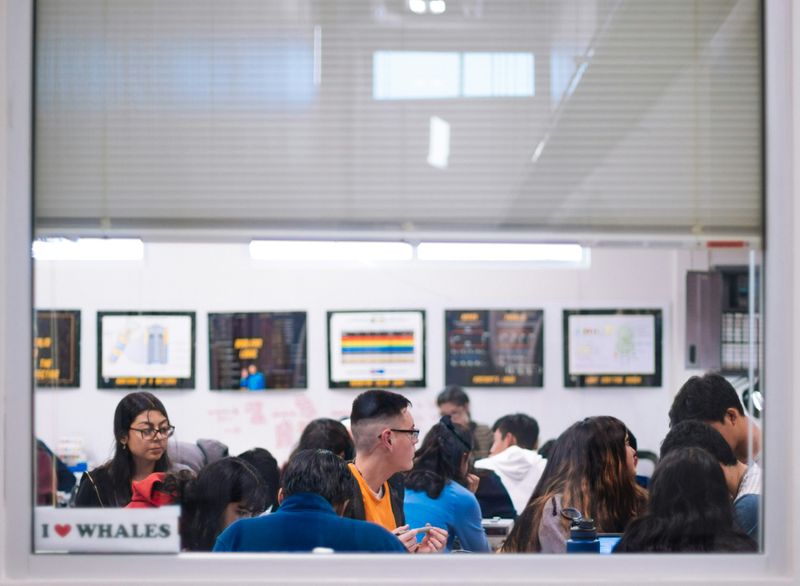 A busy school cafeteria, as students sit at tables and eat their food.