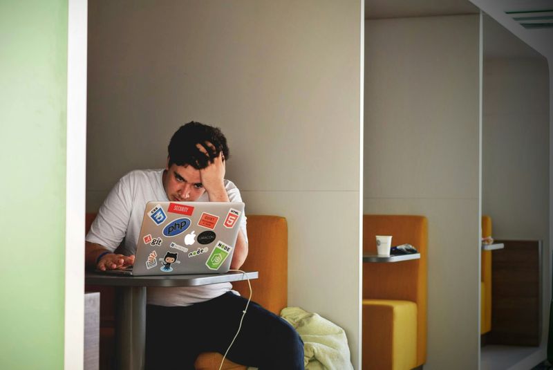 A frustrated student working on a laptop alone in a cubicle.