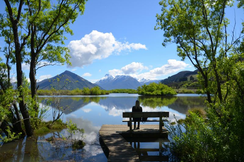 A person sitting on a bench looking out over a lake with mountains in the background.