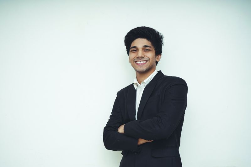 A young man smiling with arms crossed and looking into the camera.