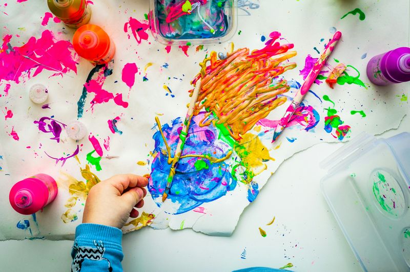 A child's hand on top of a paper with painted designs and art supplies.