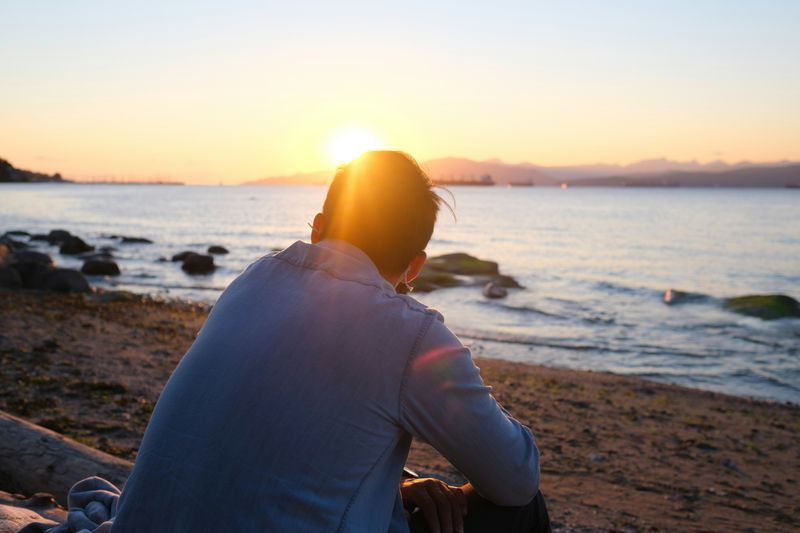 A person sitting on the beach with the sun setting in the far distance. 