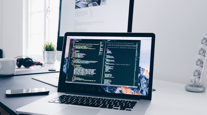 An image of a laptop on a desk with coding visible on the monitor.