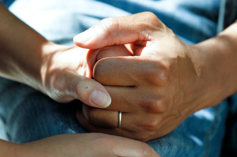 A caregiver holding someone's hand on a hospital bed