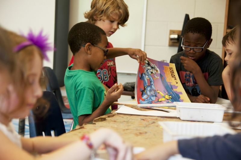 School children in a classroom, engaged and looking at a book together