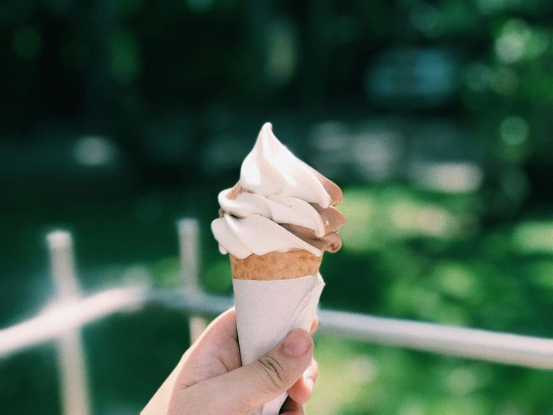 A scoop of vanilla and chocolate ice cream in a waffle cone wrapped in white paper with a green background.