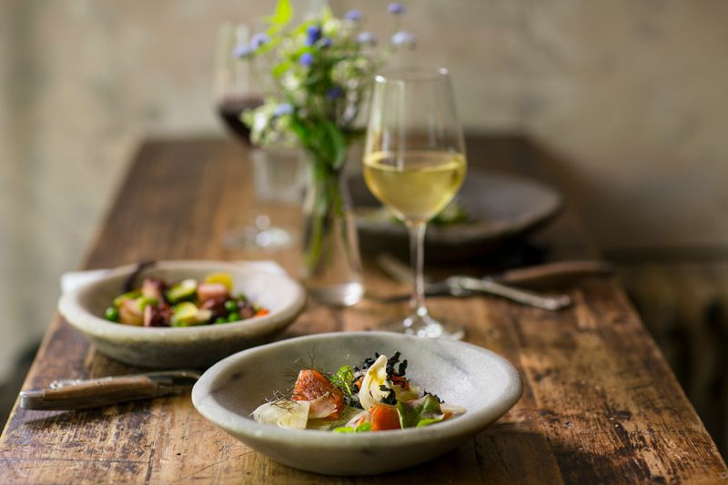 A meal of vegetables and wine served on a wooden table with a flower decoration