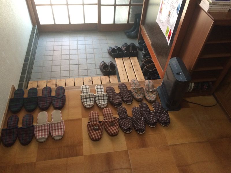 Shoes in a Japanese household beside the front door. House slippers appear in a row on a landing.