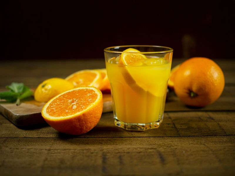 A person pouring a glass of orange juice into a cup from a large drink cooler.