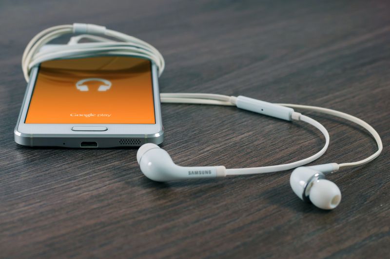 Photo of a white iPod with an orange screen partially wrapped around with white ear buds on a wood-grained table