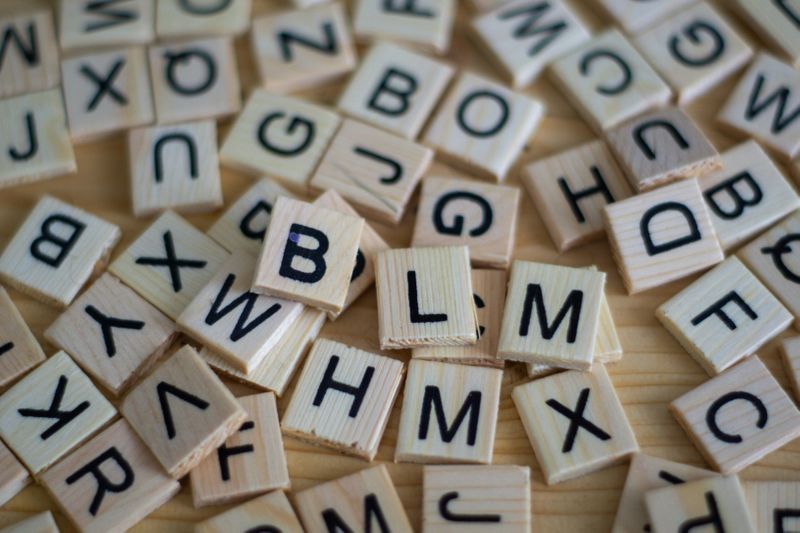 A bunch of scattered wood tiles with letters on them that look like they are from the boardgame Scrabble.