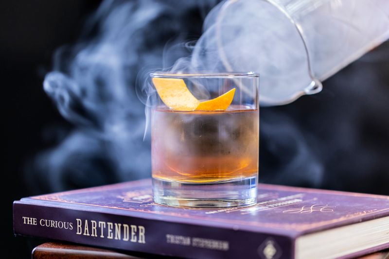 A cocktail drink with a lemon twist  on top of a book.