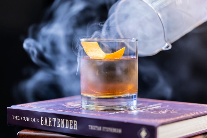 A cocktail drink with a lemon twist on top of a book.