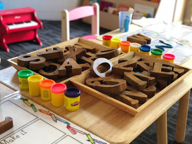 Close up image of a kids desk with wooden alphabets on trays with playdough containers on the sides