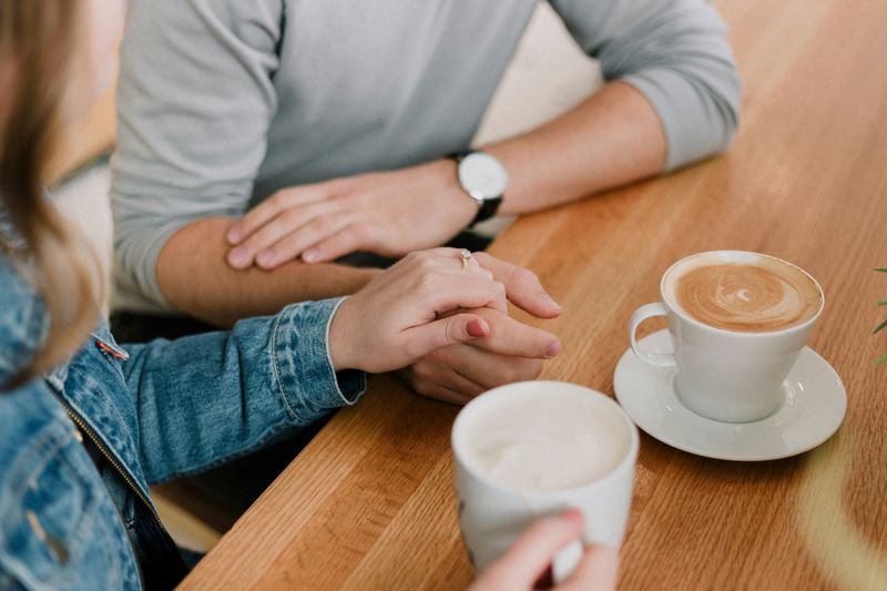 A couple sitting at a table holding hands and drinking coffee.
