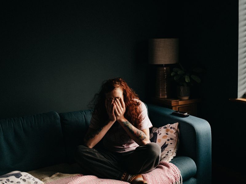 An Image of an individual with hands in face, sitting on couch. Seems tired.