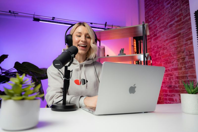 A woman speaking into a desktop microphone while using a laptop