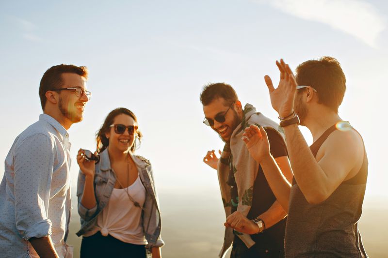 Four young friends laughing and enjoying each other's company outdoors in warm golden sunlight.