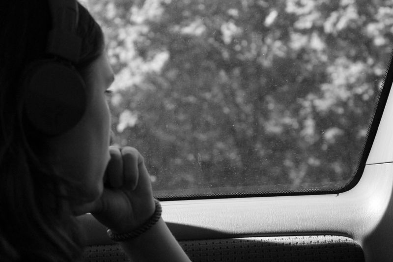 An image of a woman looking out of a car window with headphones on