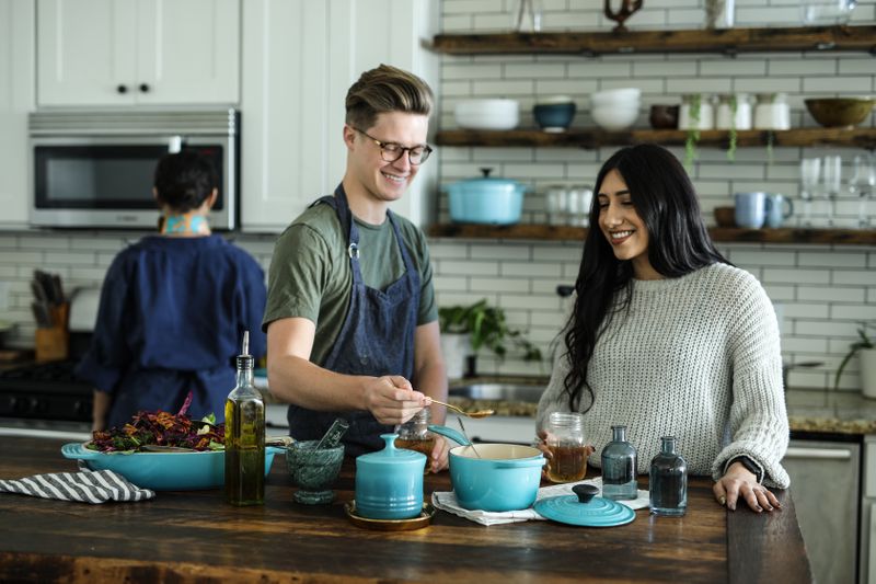 Three young people are cooking a meal in a kitchen.