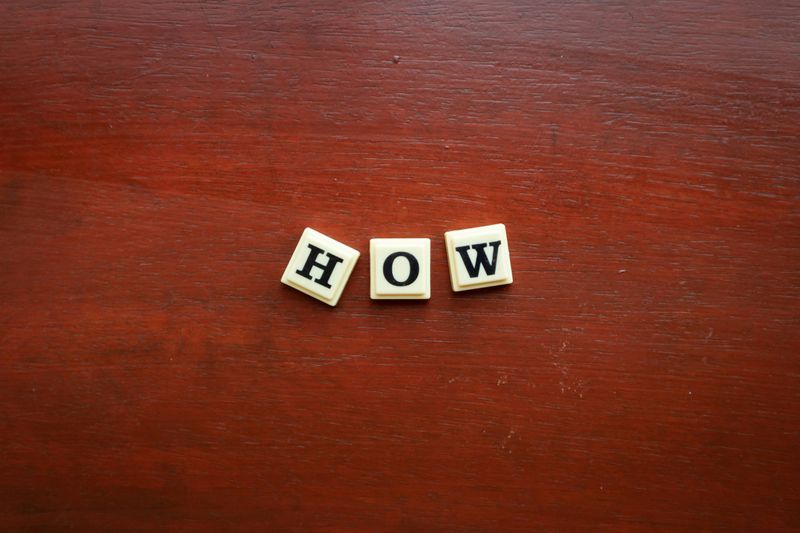 Letter blocks spell out the word "How" on a wooden table.
