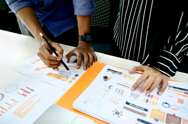 Two people doing research. They look at different infographics on a desk.