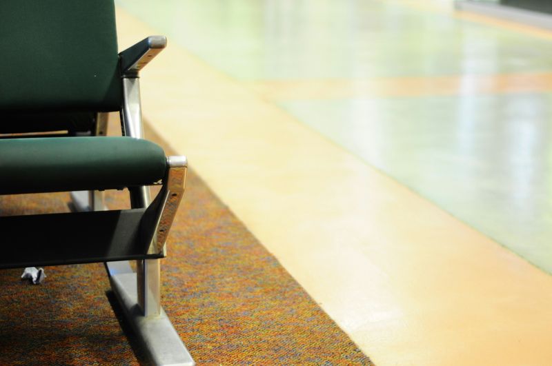 A green chair in a clinic or waiting area with a polished floor and colorful carpet.